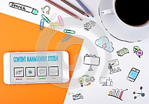 Content Management System concept. Mobile phone and coffee cup on a white office desk