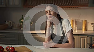 Content Woman in Apron Resting in Sunlit Kitchen With Fresh Produce