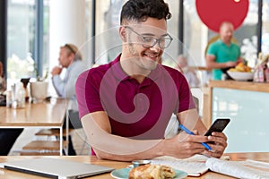 Content young male blogger holds cell phone, downloads files, sends text messages, uses free internet connection, poses