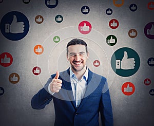 Contented businessman smiling broadly shows thumb up gesture, surrounded by multicolor like symbols. Business project approval and