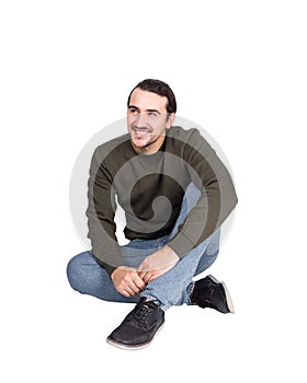 Contented casual young man sitting on the floor smiles looking aside. Lifestyle full length portrait happy student guy isolated on