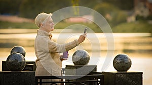 Contented middle-aged lady making video call looking at smartphone screen talking on cell phone. Elderly woman in