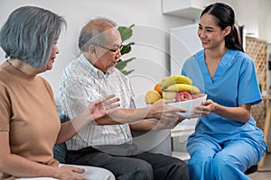 Contented senior couple taking a bowl of fruit from a nurse at home.