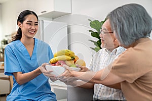 Contented senior couple taking a bowl of fruit from a nurse at home.