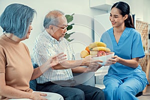 Contented senior couple taking a bowl of fruit from a nurse at home.