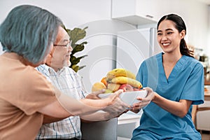 Contented senior couple taking a bowl of fruit from a nurse at home.