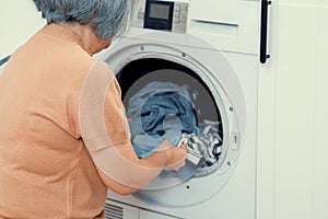 Contented senior housewife doing laundry in the laundry room.