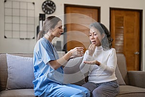 Contented senior woman taking medicines while her caregiver advising her medication. Medication for seniors, nursing