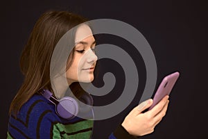 Contented smiling girl typing text message or scrolling through social networks using smartphone.