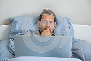 Contented young businessman freelancer work on laptop laying in bed at home. Male professional trader investor working
