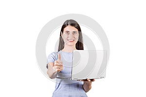 Contented young woman holding a laptop in her hand while showing thumb up positive gesture to camera, isolated on white background