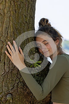 Contented young woman hugging a large tree with a blissful expression and her eyes closed in a concept of save the