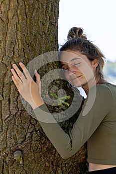 Contented young woman hugging a large tree with a blissful expression and her eyes closed in a concept of save the