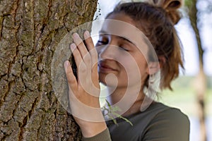 Contented young woman hugging a large tree with a blissful expression and her eyes closed in a concept of save the