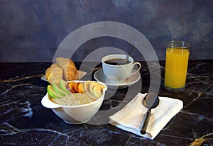 Continental breakfast, a cup of oatmeal with slices of fruit, orange juice, black coffee and two fresh croissants on a plate