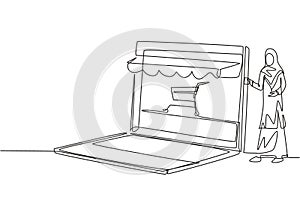 Continuous one line drawing young Arab woman inserting credit card into canopy laptop screen with shopping cart. E-shop, digital