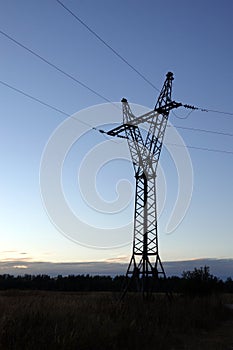 Contour of high-voltage strong power line metal prop with electrical wires in twilight on beautiful rural sunset