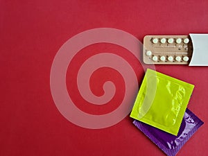 Contraceptives condom and contraceptive pills on red background