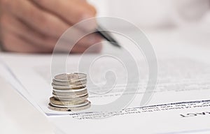 Contract signing concept. Businessman hand with pen over document closeup. money coins in focus on foreground