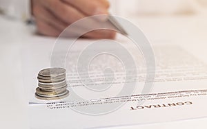 Contract signing concept. Businessman hand with pen over document with coins in focus in foreground