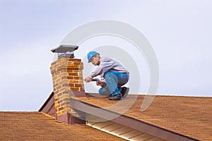 Contractor Builder on roof with blue hardhat caulking chimney photo