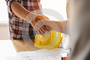 Contractor and engineer shaking hands after deal to renovation building is complete and blueprint is reviewed