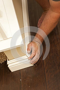 Contractor Fitting New Baseboard to Wall and New Laminate Flooring