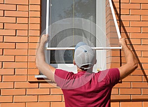 Contractor installing mosquito wire screen on house window to protect from insects. Mosquito wire screen installation