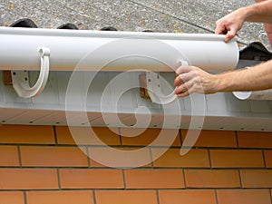 Contractor installing plastic roof gutter. Plastic Guttering Replace, Rain Guttering & Drainage Repair by Handyman hands.