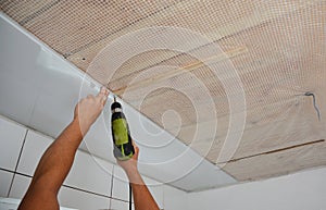 Contractor installing white PVC Ceiling Boards with screw gun in the bathroom