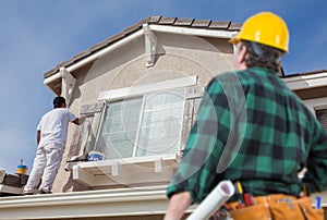 Contractor Overlooking Painter Painting House