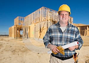 Contractor with Plans and Hard Hat In Front of New House Framing