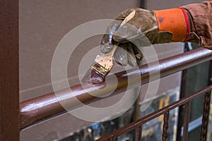 Contractor`s hand with brush that painting metal railing construction.