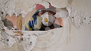 Contractor in uniform, harhat shows thumb up sign in a wall hole and has fun on apartment rearrangement works. Man doing