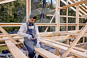 Contractor Working With Drill Driver. Carpenter Working on Wooden House Skeleton Frame