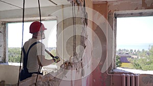Contractor wrecks wall with sledgehammer making hole for rearrangement. Construction worker doing manual dismantling and