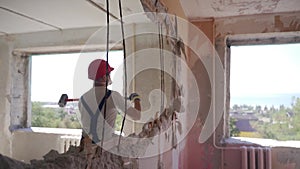 Contractor wrecks wall with sledgehammer making hole for rearrangement. Construction worker doing manual dismantling and