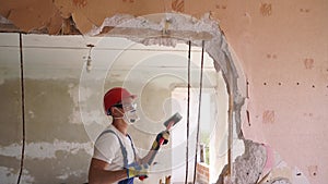 Contractor wrecks wall with sledgehammer making hole for rearrangement. Man doing manual dismantling and demolition