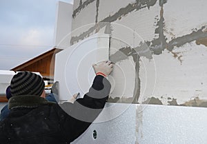 Contractors installing rigid styrofoam insulation board on house construction wall. House insulation outdoors