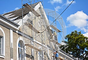 Contractors plastering house facade outdoor. Painting and plastering exterior house scaffolding wall with asbestos roof repair