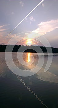 Contrails in the sky play in waves in the forest lake