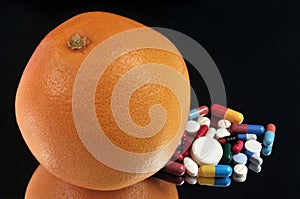 Grapefruit next to an assortment of drugs on a black background