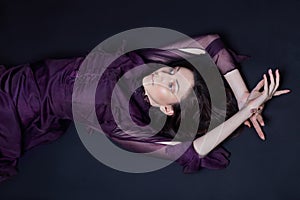 Contrast fashion Armenian woman portrait with big blue eyes lying on the floor in a purple dress. Lovely gorgeous girl posing