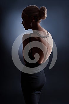 Contrast fashion woman portrait on dark background, the silhouette of a girl with a beautiful curved back. Naked back of a woman