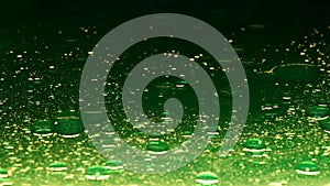 Contrast green colored water surface with golden oil droplets moving, abstract background. Slow motion.