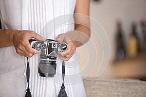 Contrast between old and modern times: a young woman with a vintage camera around her neck fiddles with her smartphone photo