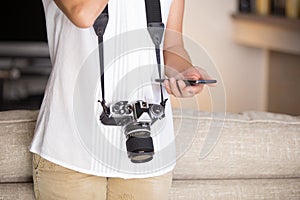 Contrast between old and modern times: a young woman with a vintage camera around her neck fiddles with her smartphone photo