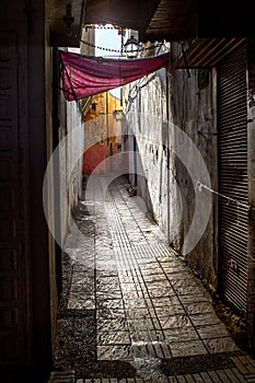 Contrast Sale Morocco. The narrow street of the old city and the old, chipped walls of houses under a red canopy in the summer