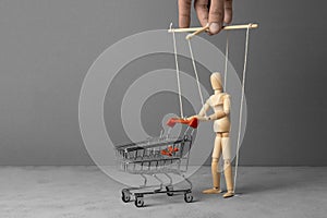 Control over the behavior of the buyer. Man with a shopping trolley from the supermarket like doll led by puppeteer. Copy space