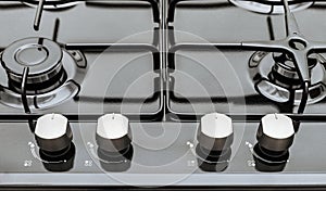 Control panel of a black gas cooktop with four silver knobs